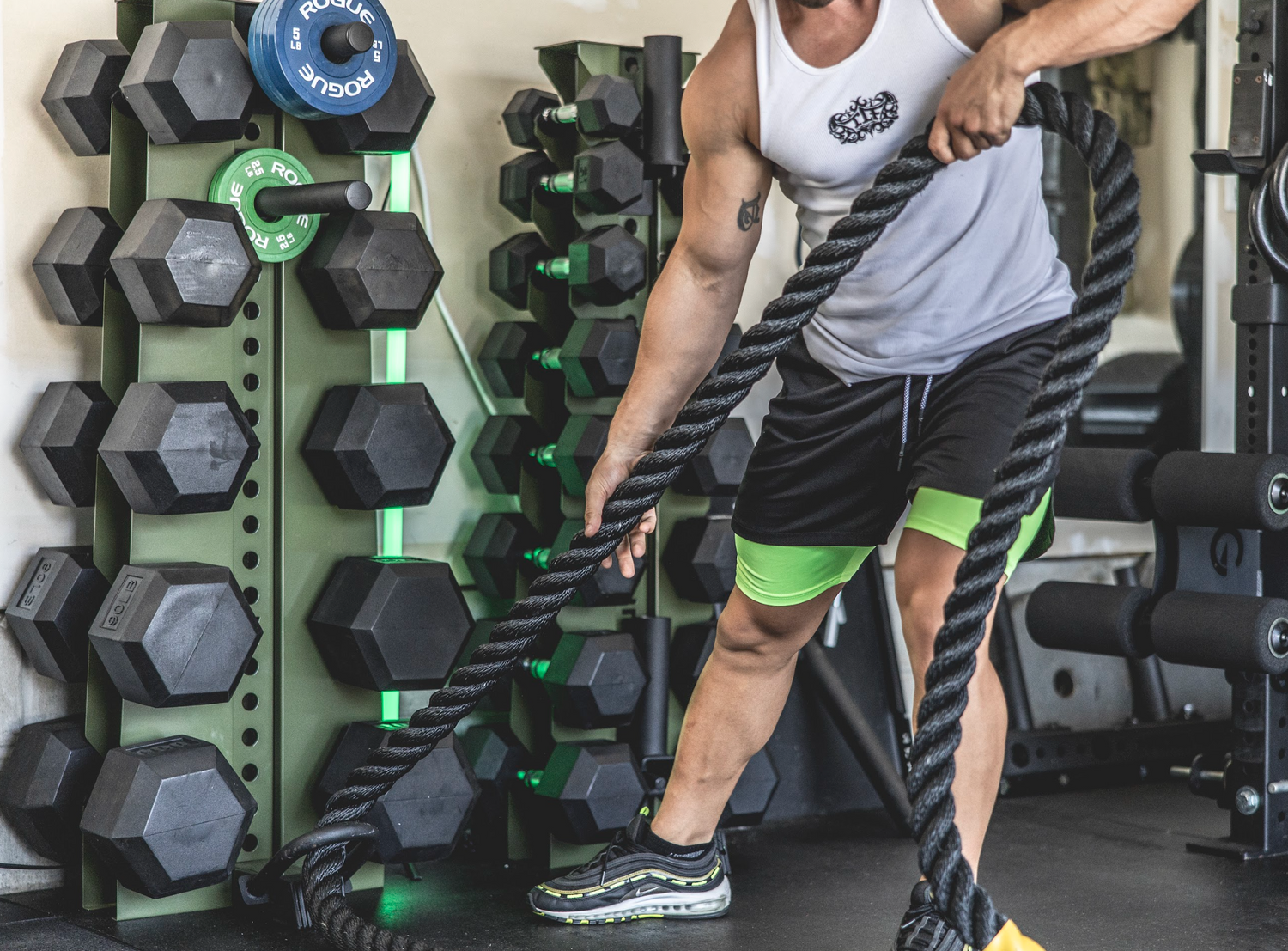 a man putting a battle rope on his vertical dumbbell rack to finish building his home gym