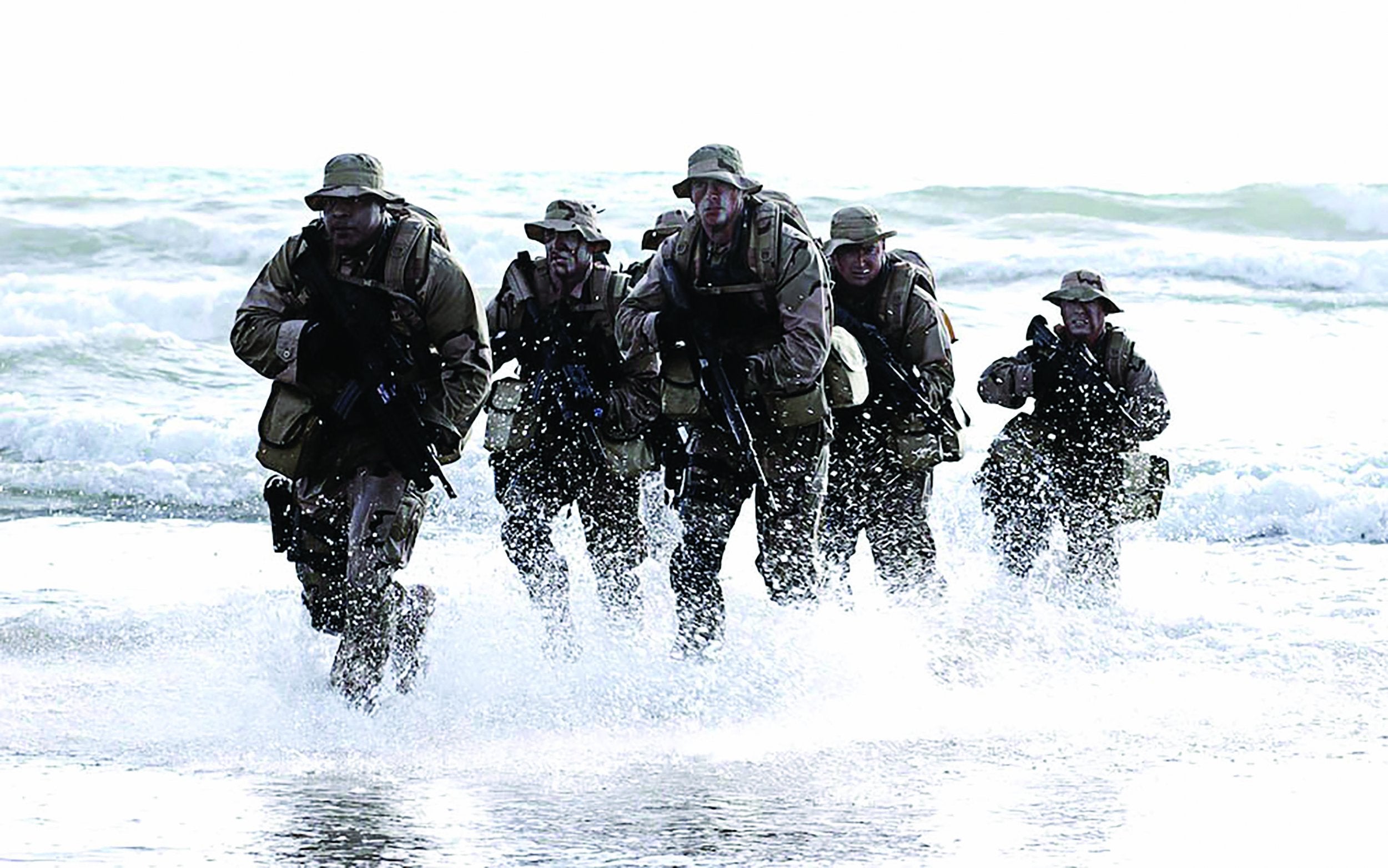 military men with guns and full gear running out of the water on a beach.