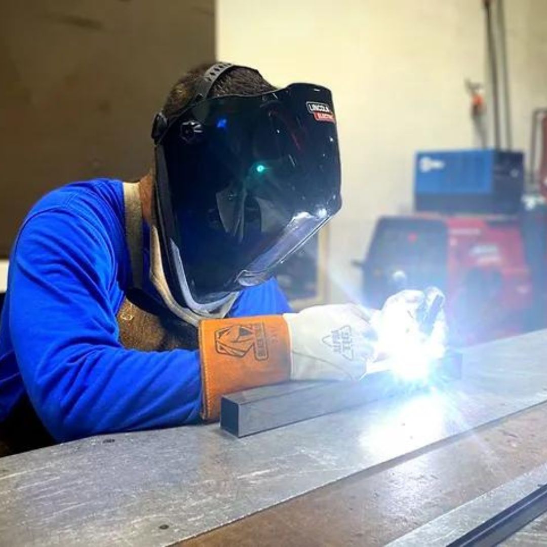 a worker welding a metal part of the base of a Synergy Custom Fitness dumbbell rack.
