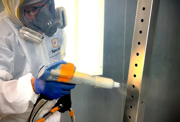 a worker powder coating an upright for a Synergy Custom Fitness dumbbell rack.