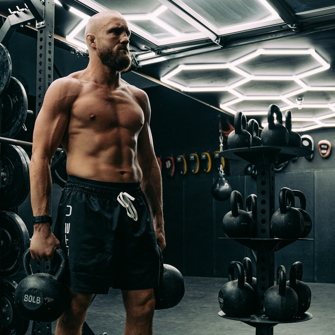 man in a gym holding kettlebells with other gym equipment around him