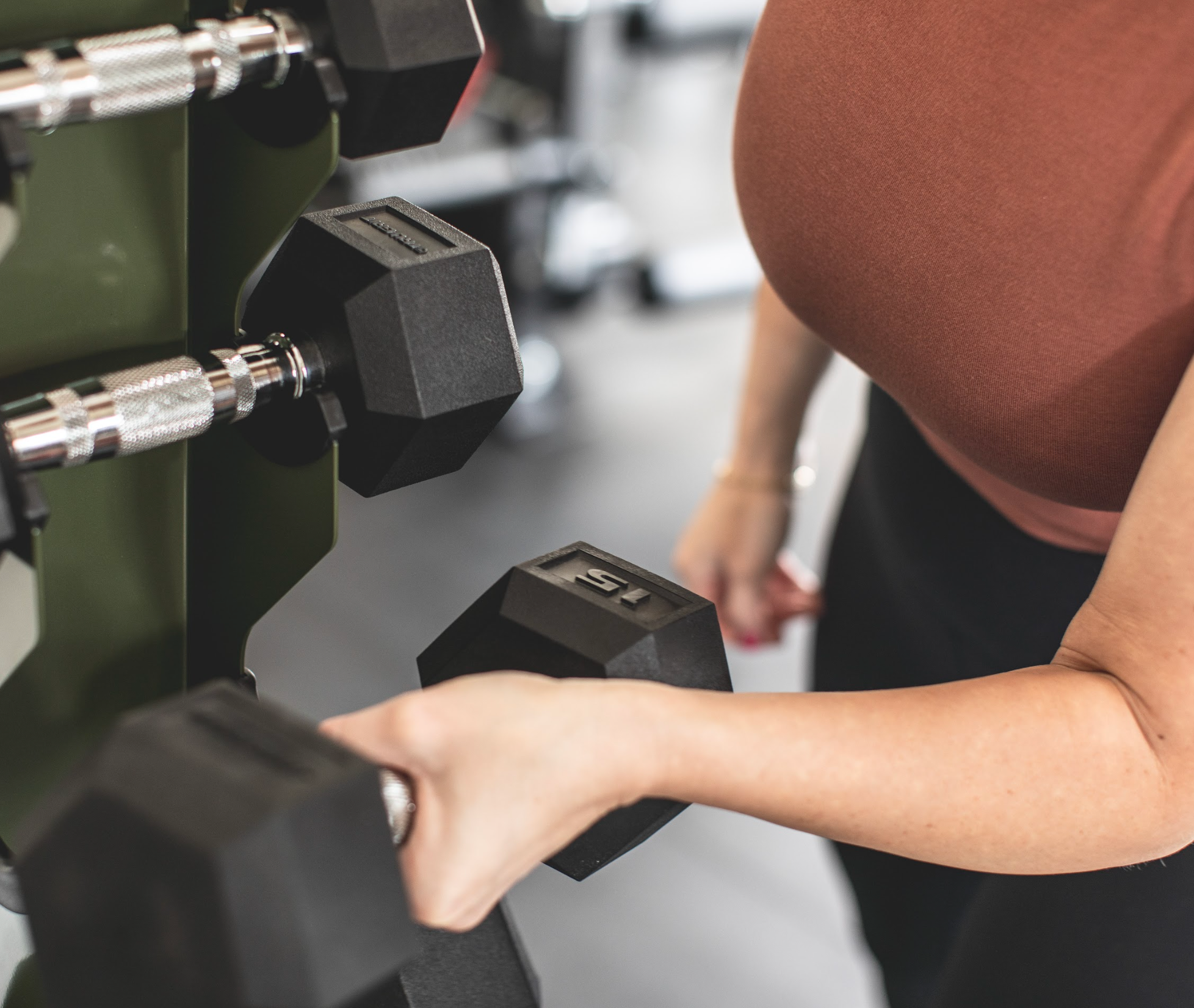 woman taking a dumbbell off a vertical dumbbell rack