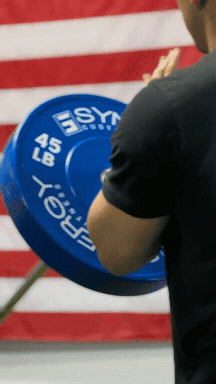 a short video of a man doing landmine workouts using a barbell connected to a white 8-tier vertical dumbbell rack with a landmine accessory.