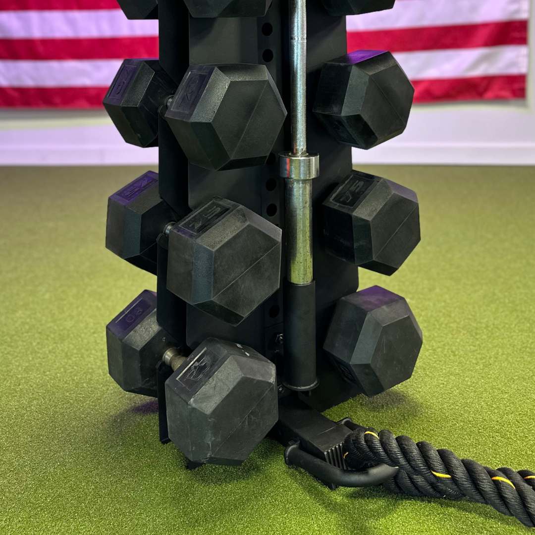 the base of a black vertical dumbbell rack holding dumbbells, a barbell being help by a barbell holder accessory, and a battle rope being held by a battle rope accessory.